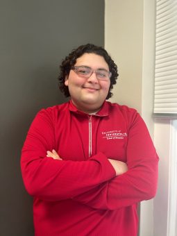 Dylan Torres, a recent graduate of the University of Indianapolis, poses for a photo. He wears a crimson quarter-zip polo bearing the UIndy School of Education logo.