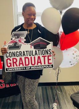 Que Cooper, recent graduate of the University of Indianapolis poses for a photo. She holds a sign that reads "Congratulations Graduate, University of Indianapolis."
