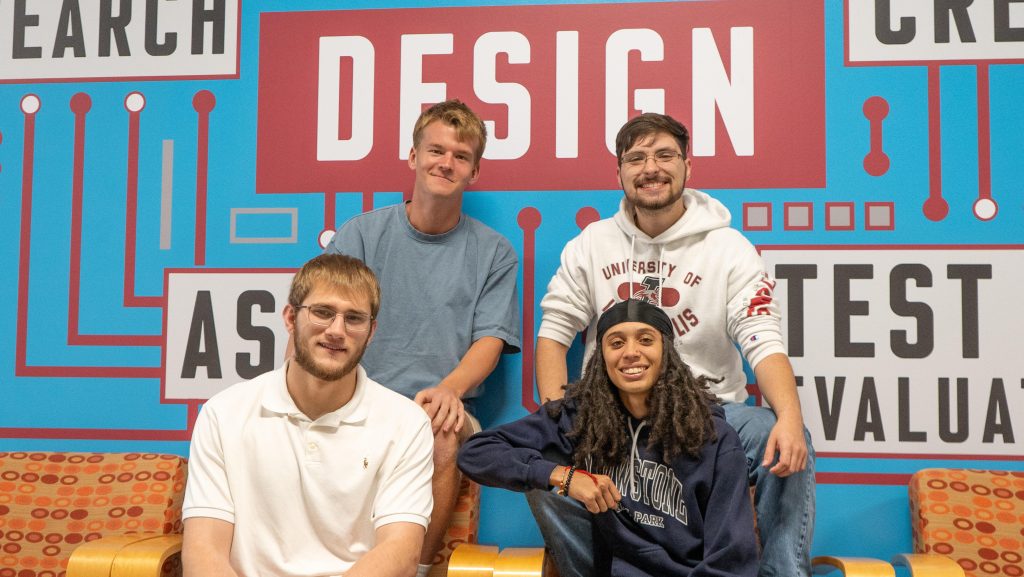 Four engineering students smile in front of UIndy DesignSpine artwork