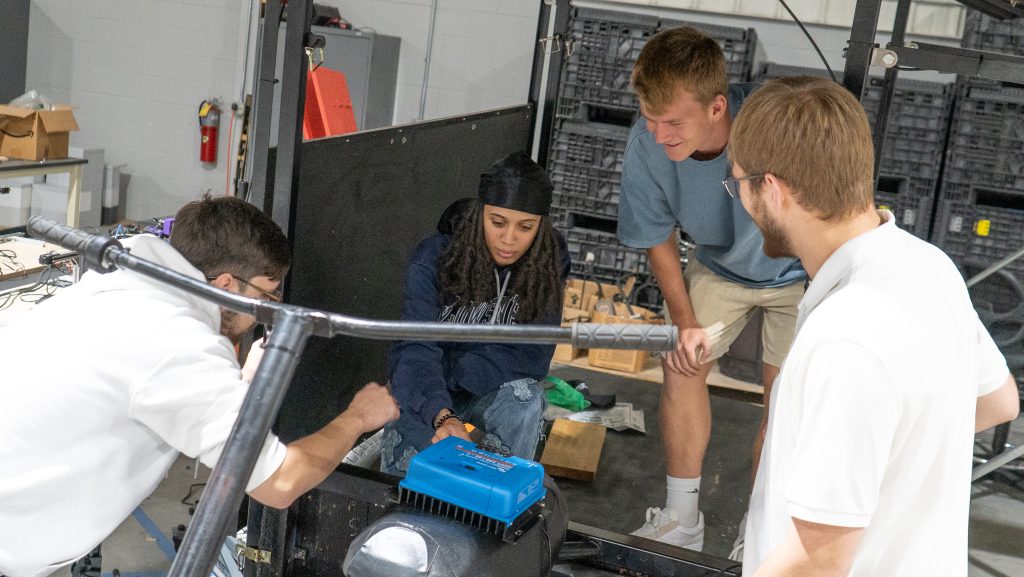 Four engineering students work together on a vehicle engine 