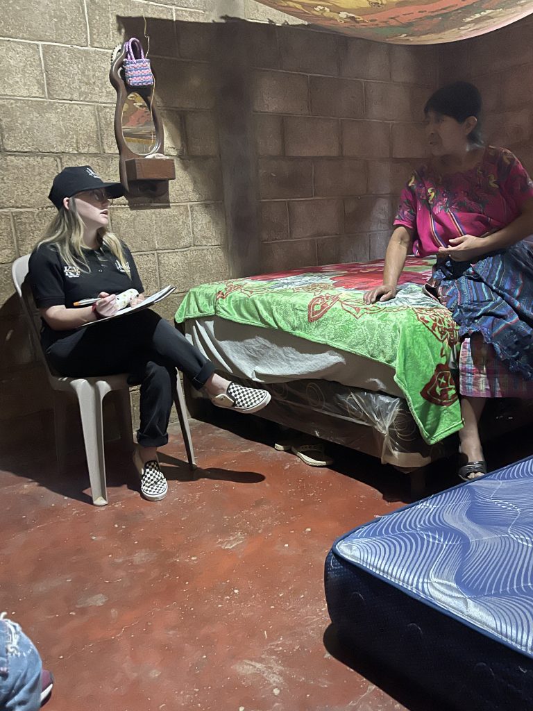 Woman sitting down takes notes in bedroom while another listens 