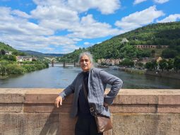 Man stands at riverfront, with scenic landscape with green picturesque trees and blue skies