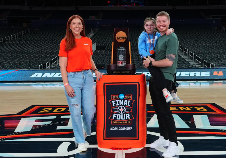 Woman, man and girl stand on basketbakk court with large championship trophy sitting on a podium between them