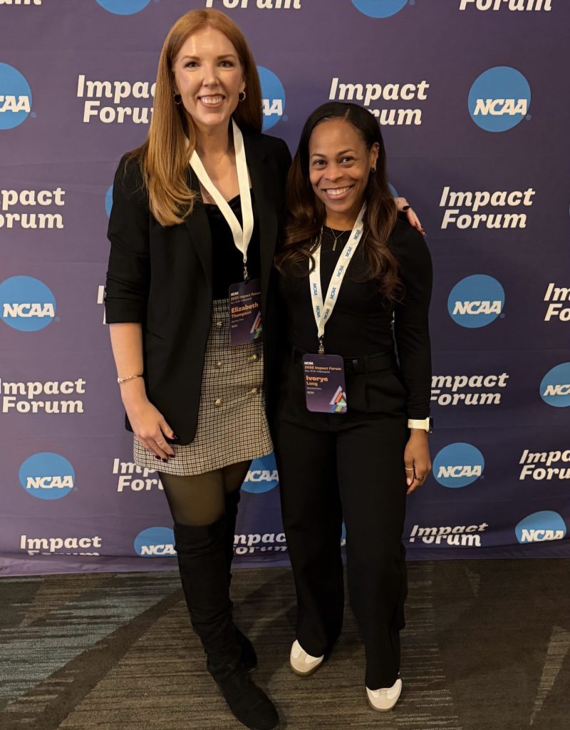Two women in professional attire stand in front of blue backdrop with NCAA logo and words "Impact Forum"