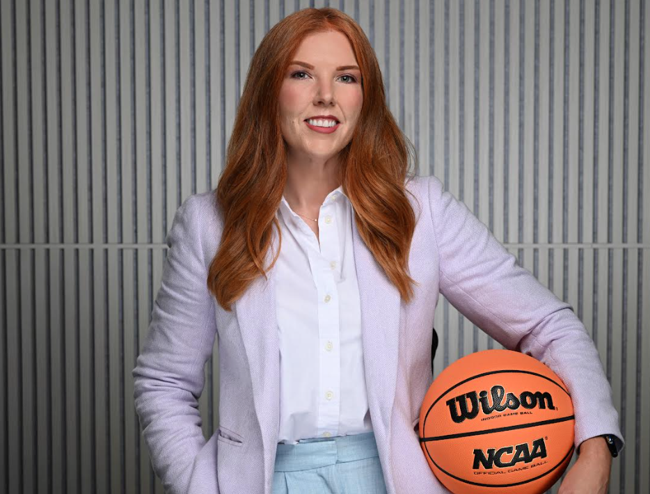 Woman smiles for camera wearing professional attire, holding basketball